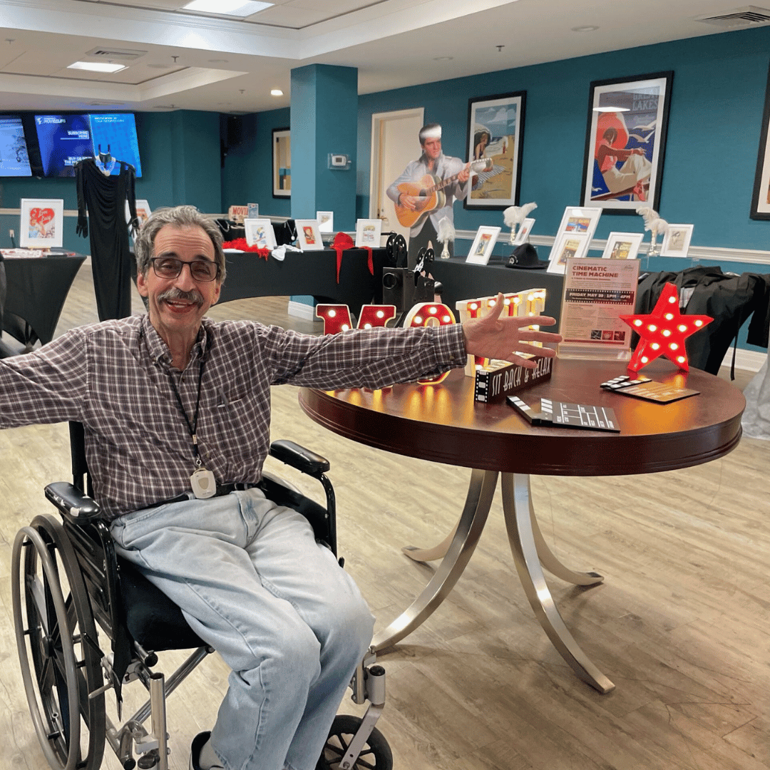 Senior Westbury resident smiles and poses in front of multiple film exhibits at the event at The Bristal