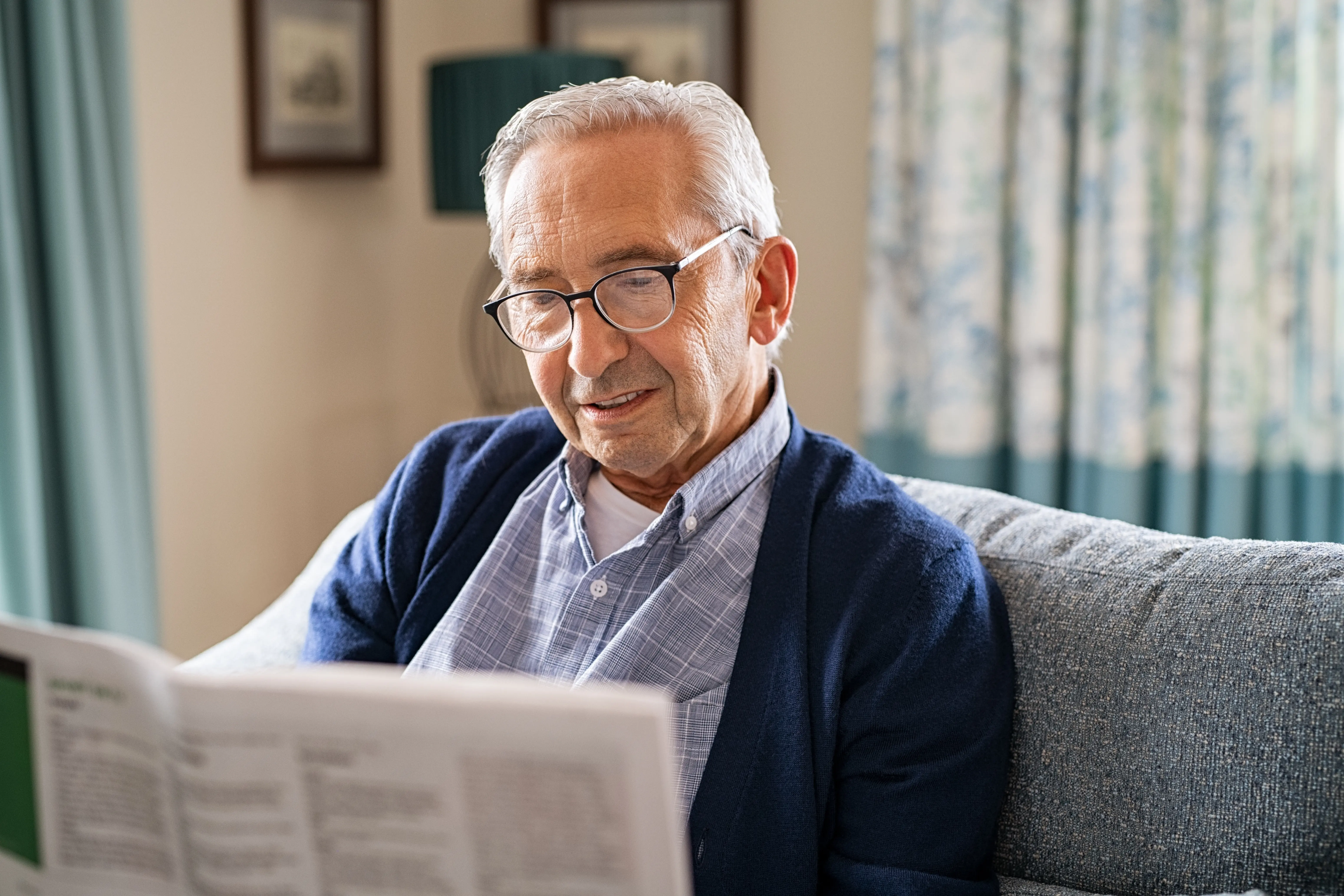 Older male resident of The Bristal Assisted Living relaxes while reading a newspaper