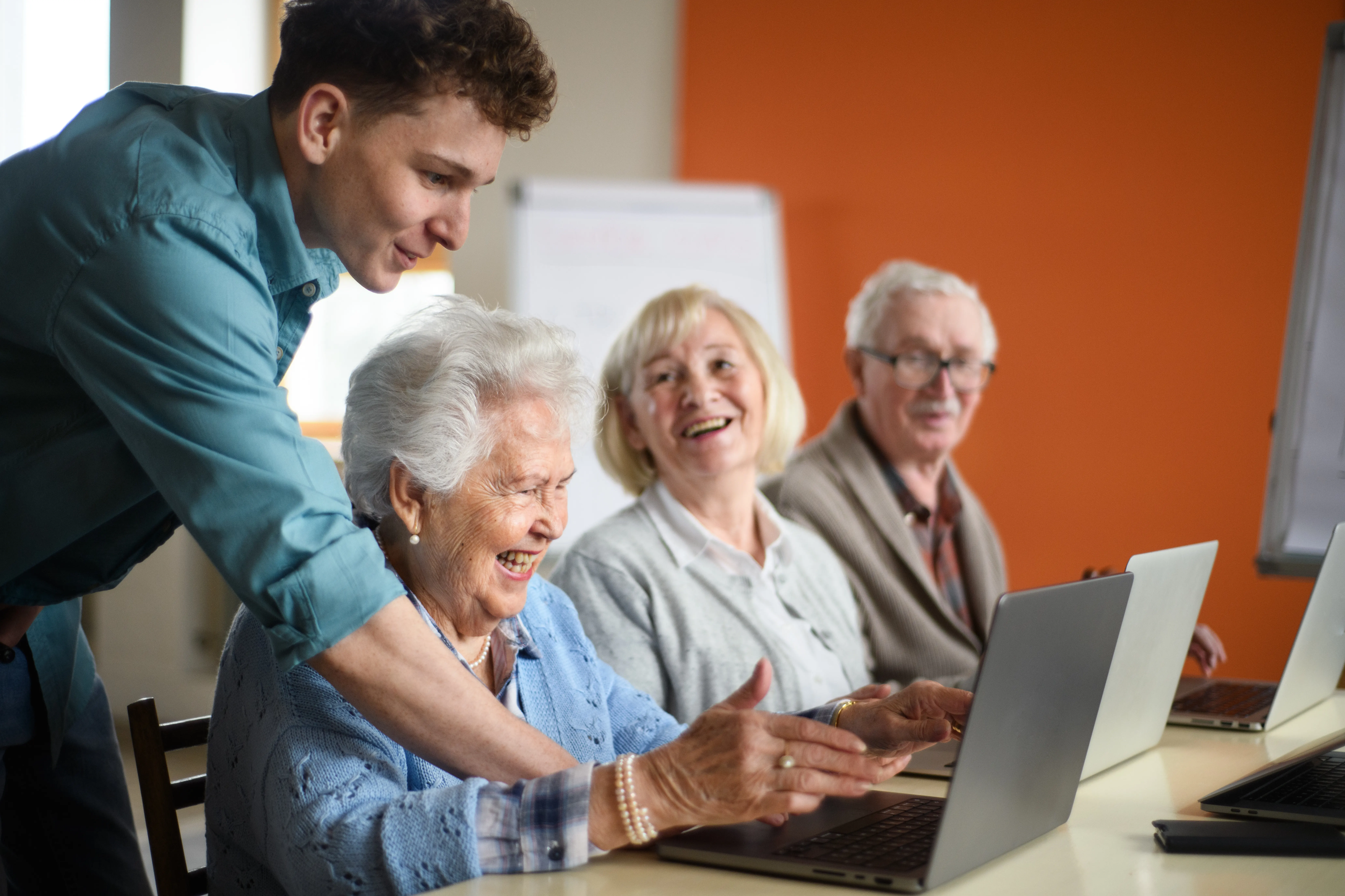Residents of The Bristal sit together looking at laptop computers while a team member of The Bristal assists them